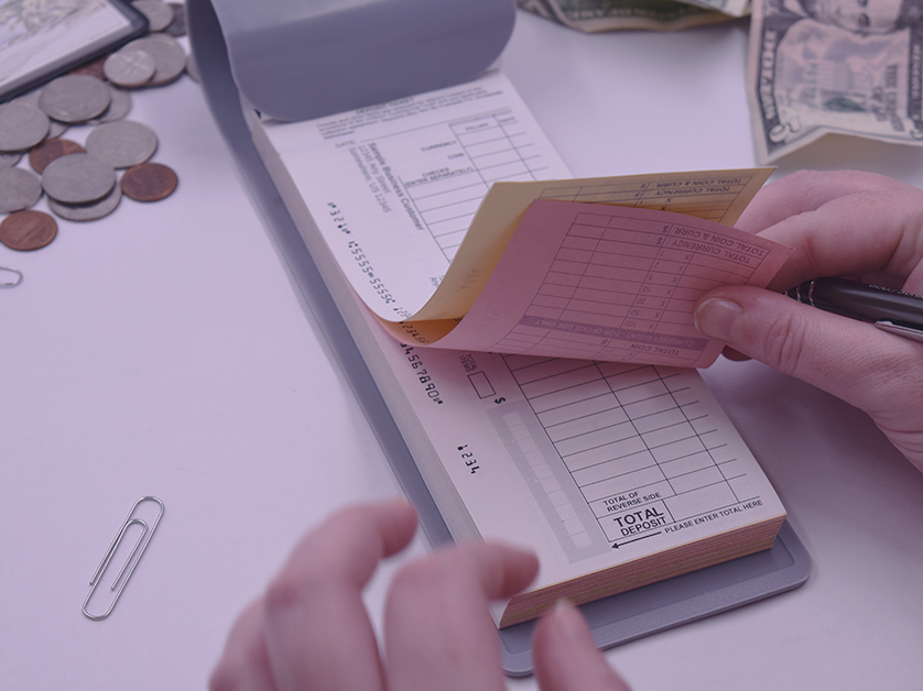 A pad of deposit slips, being filled out by a pair of hands holding a pen.
